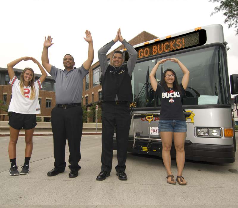 people standing in front of bus, signaling O-H-I-O with hands