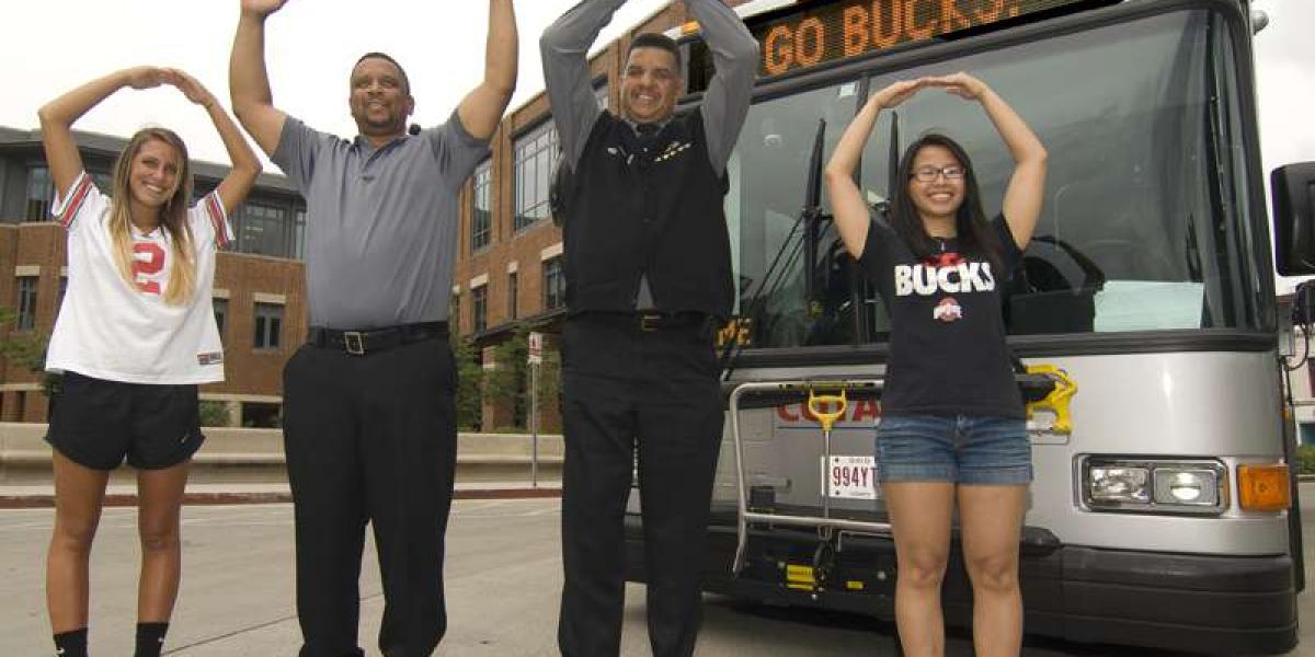 people standing in front of bus, signaling O-H-I-O with hands