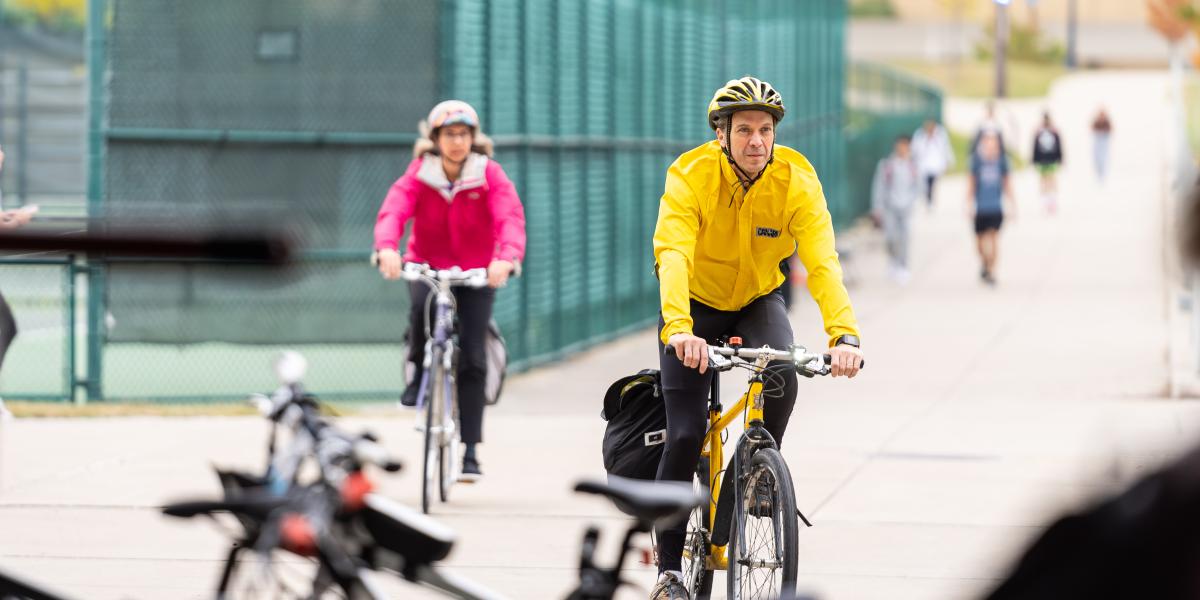 A man in a bright yellow jacket and woman in pink jacket are seen riding bicycles.