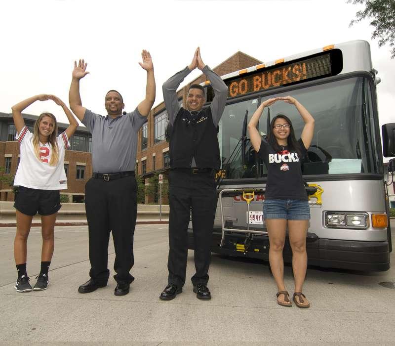 people standing in front of bus, signaling O-H-I-O with hands
